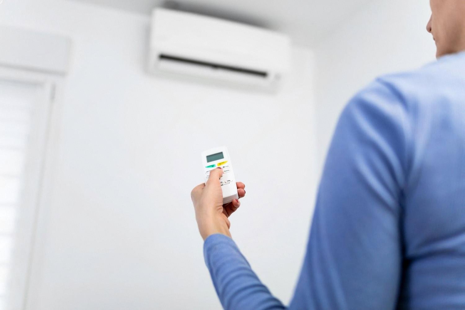 Man adjusting a wall-mounted air conditioner with a remote inside a UAE home