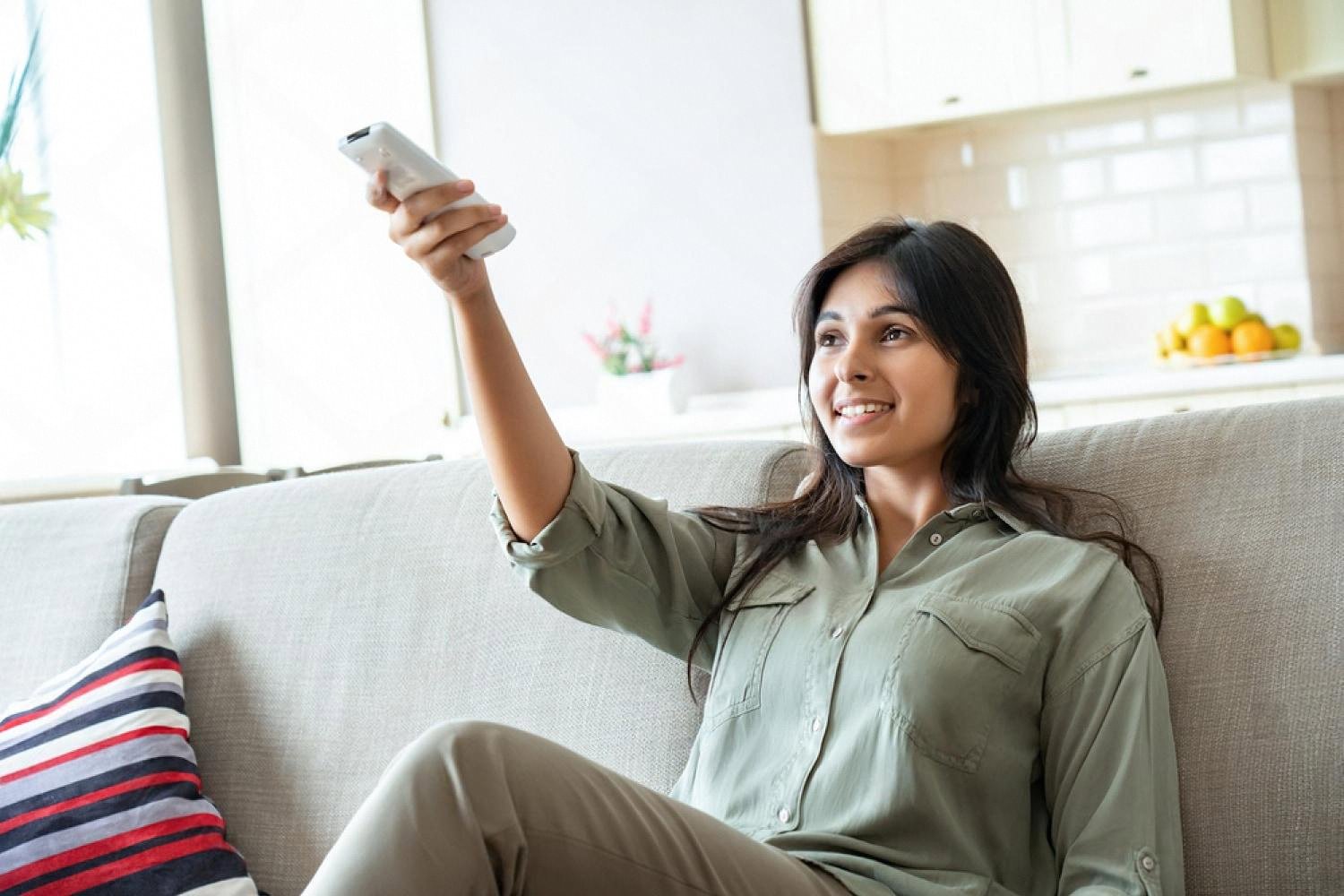 Young woman on a sofa using an AC remote in a cool Dubai living room